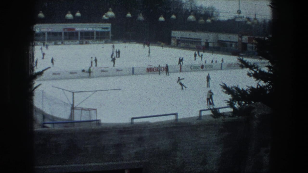 1976 Zurich outdoor rink scene with skaters spread across the ice, distant signage, railings, and dark trees at the edge.