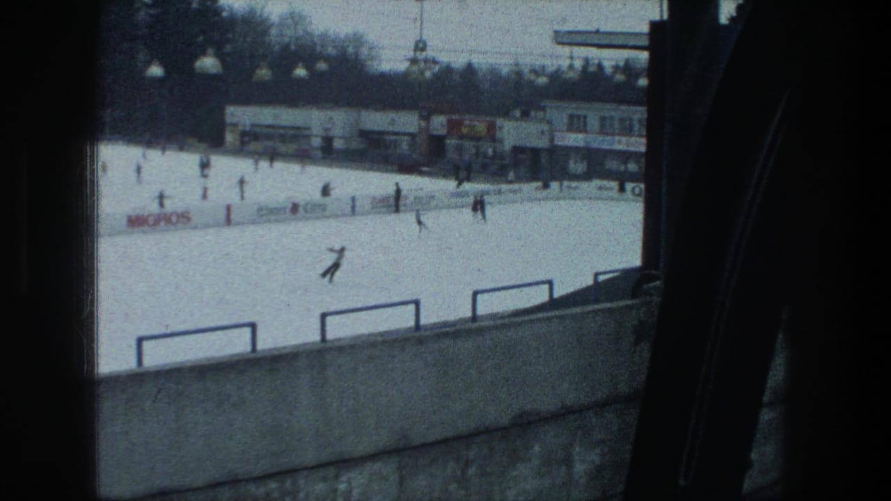 1976 Zurich rink frame with a skater in the foreground area, other people on the ice, railings, lamps, buildings, and Migros signage.