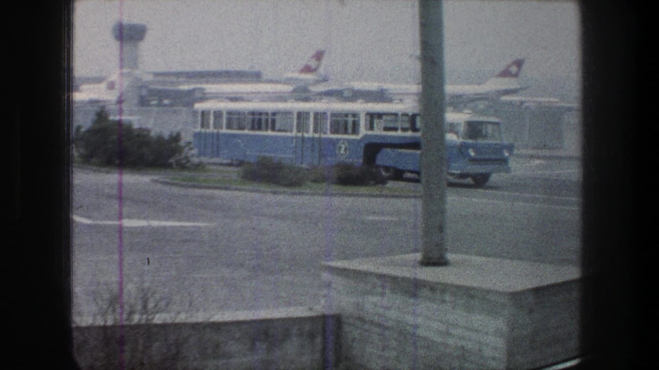 Blue shuttle bus on the airport roadway with parked jets and a control tower in the background.