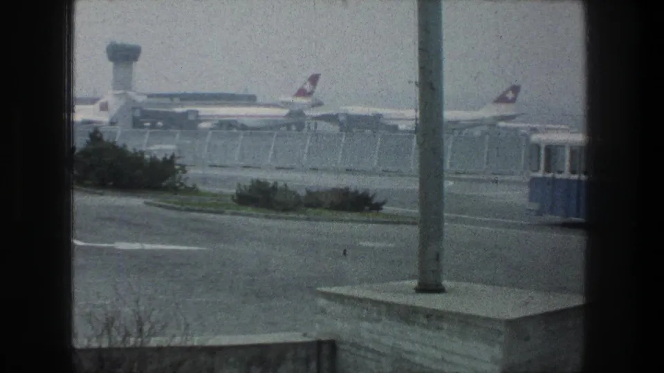 End of a 1976 Zurich airport view with parked Swissair-marked aircraft, control tower, and the shuttle bus nearly out of frame.