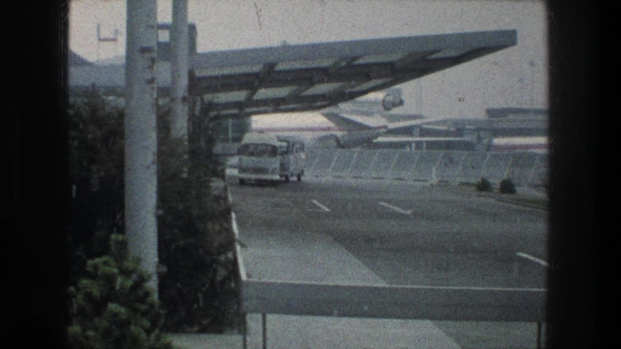 1976 Zurich airport view with a white bus on an access road, a modern canopy overhead, and jet aircraft visible past the fence.