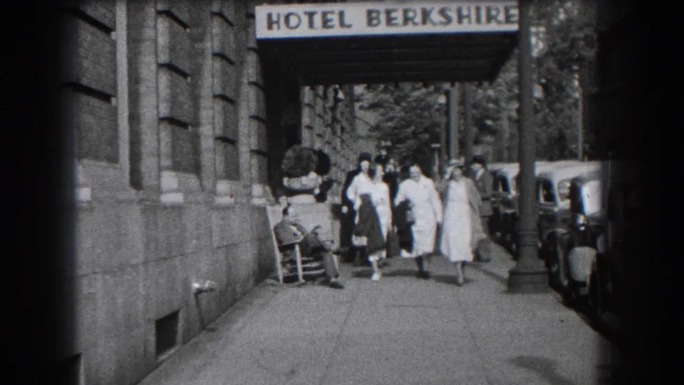 Women in period hats and light coats walk from the Hotel Berkshire entrance in Reading, Pennsylvania, with 1930s cars nearby.