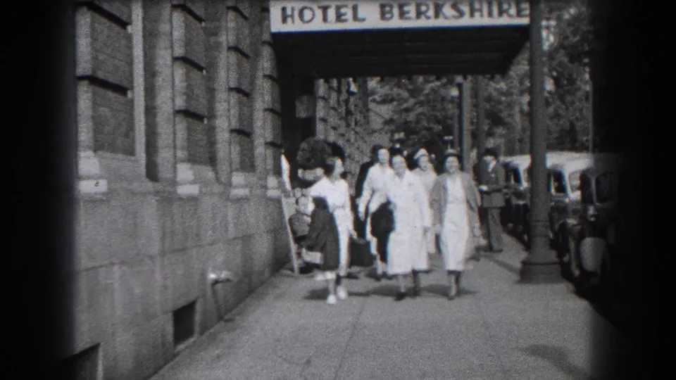 The group advances down the sidewalk outside the Hotel Berkshire in Reading, Pennsylvania, framed by the awning and curbside cars.