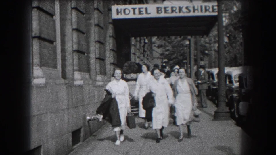 Women in nurse-style white coats and dresses walk together on a Reading sidewalk with the Hotel Berkshire sign above them.