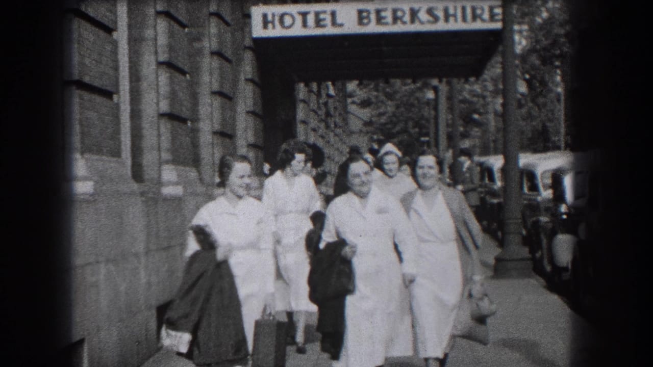 Close sidewalk frame of smiling women in nurse-style dress near the Hotel Berkshire sign, with vintage cars visible along the curb.