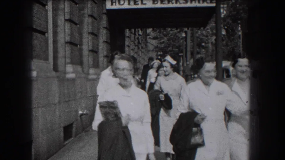 Uniformed nurses and other pedestrians move along the sidewalk under the Hotel Berkshire sign in Reading, Pennsylvania.