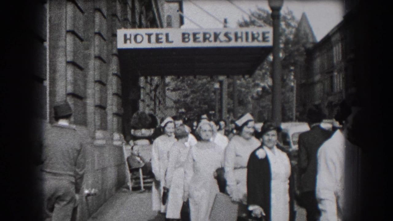 A group of nurses in white uniforms and caps walks near the Hotel Berkshire entrance, with sidewalk activity behind them.