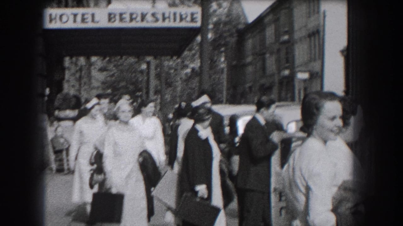 Nurses in white uniforms pass close to the camera outside the Hotel Berkshire, with pedestrians and parked cars in the background.
