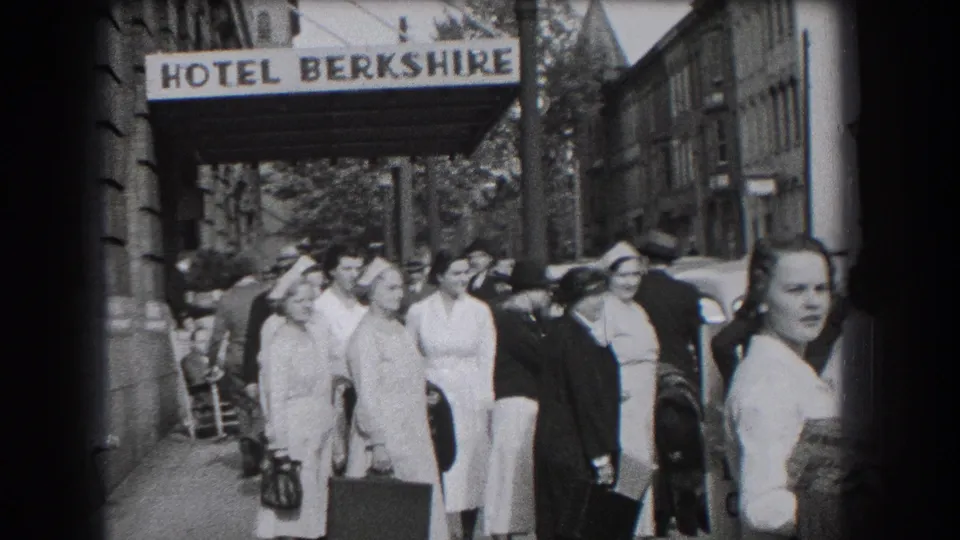 1938 hotel-side sidewalk view in Reading showing uniformed women with bags, a nearby car, and pedestrians at the curb.