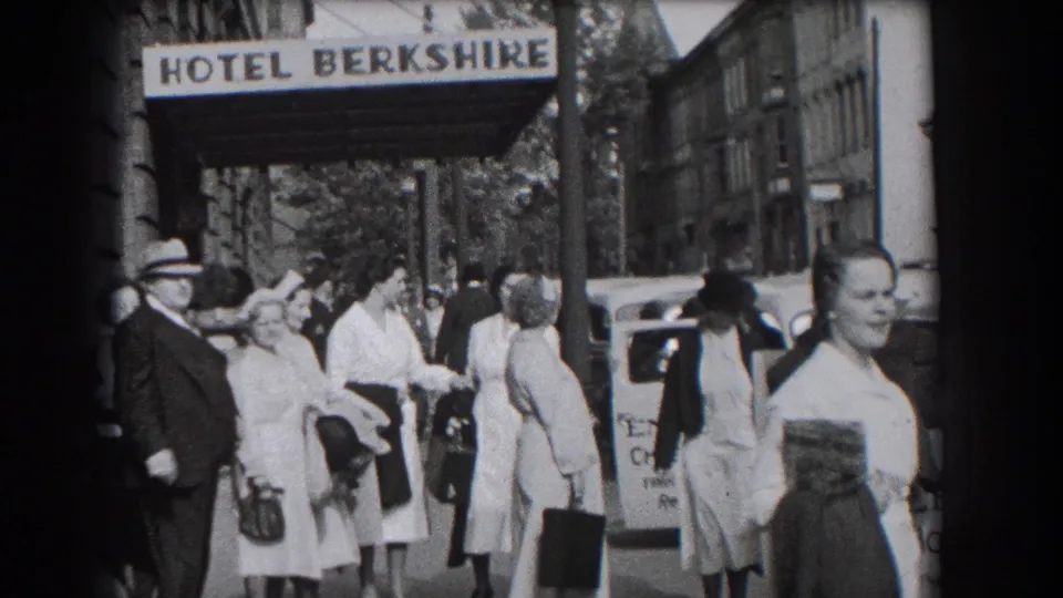 Crowded sidewalk outside the Hotel Berkshire in Reading, Pennsylvania, with passersby, luggage, cars, and storefront edges visible.