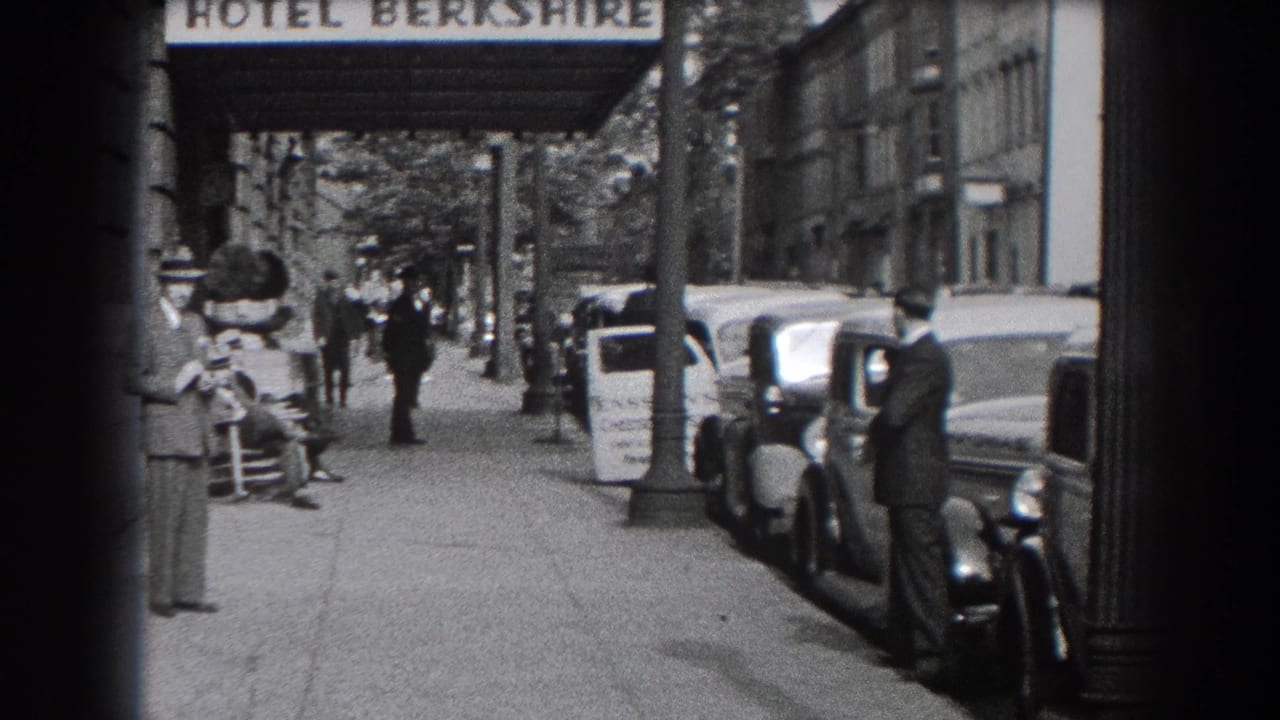 Hotel Berkshire sidewalk with pedestrians, parked cars, and men standing near the curb.