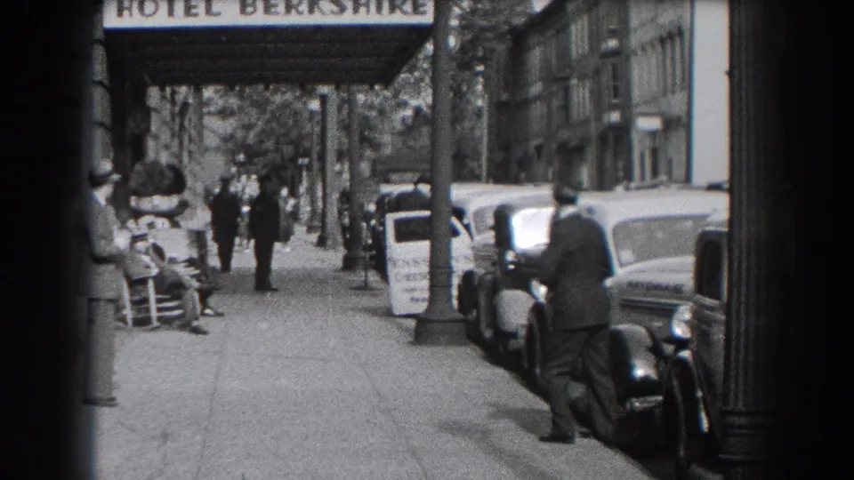 Reading street scene outside the Hotel Berkshire, showing pedestrians, vintage cars, and a man standing by a parked automobile.