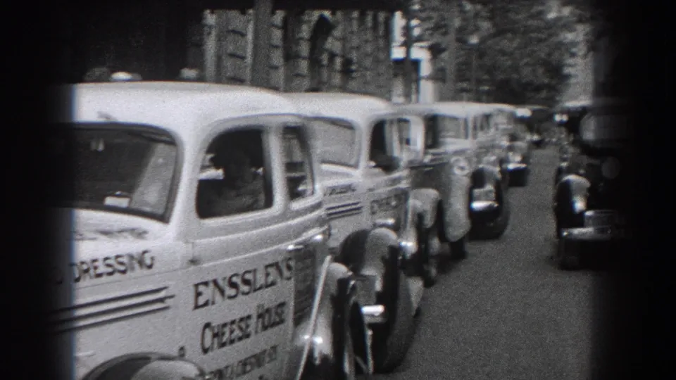 Curbside view in Reading with vintage automobiles and an Ensslen's Cheese House delivery van moving or parked near the camera.