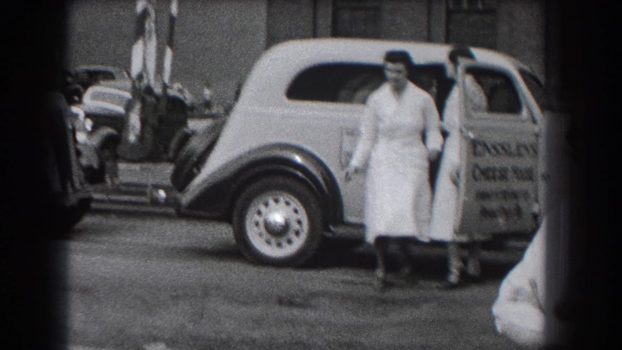 In Reading, Pennsylvania, women in white uniforms move beside a 1930s Ensslen's Cheese House delivery car on a city street.