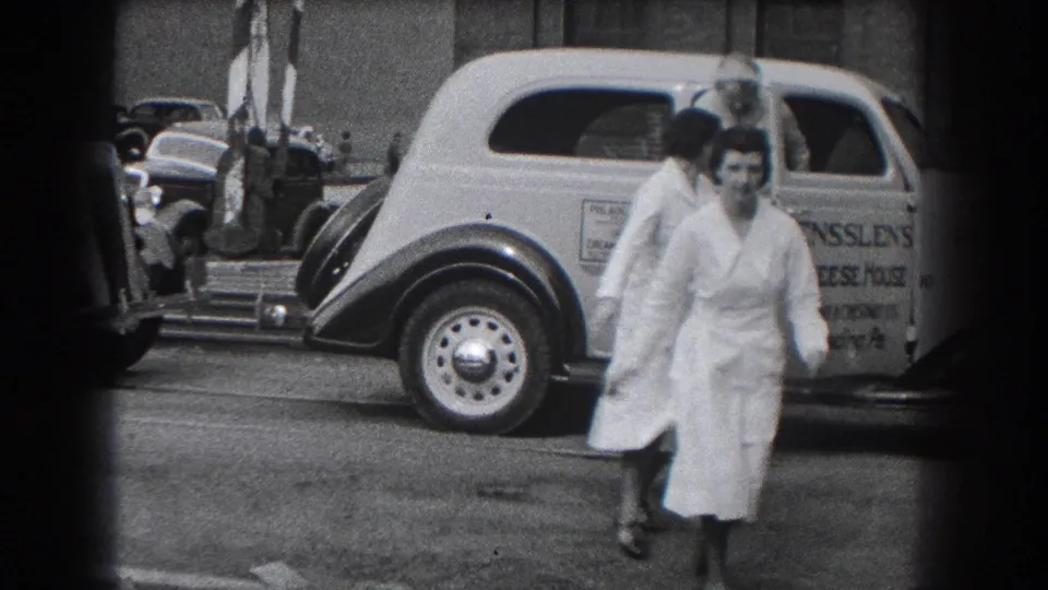 A woman in a white uniform hurries past a 1930s delivery car marked for Ensslen's Cheese House in Reading, Pennsylvania.