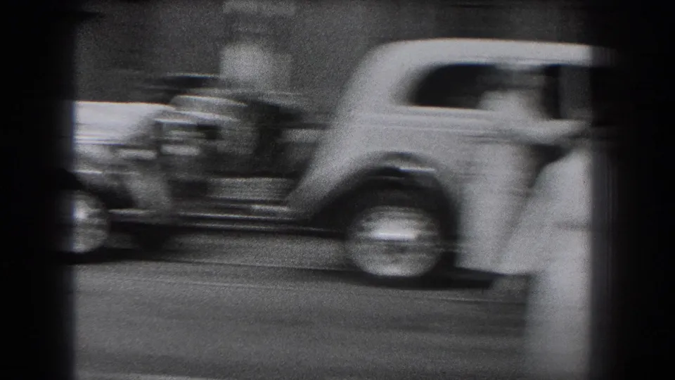 Motion blur from a passing vintage delivery car partially obscures a uniformed figure on the Reading street scene.