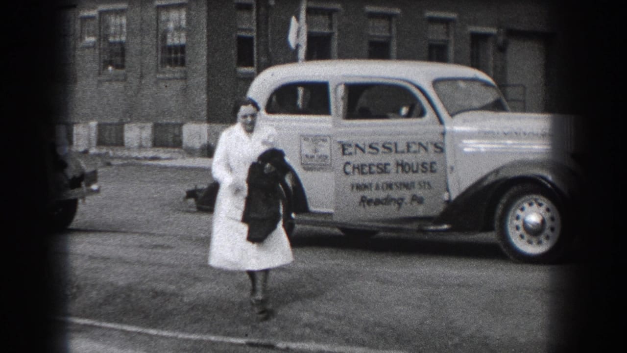 In Reading, Pennsylvania, a woman in a white dress walks near a parked Ensslen's Cheese House delivery car on a city street.
