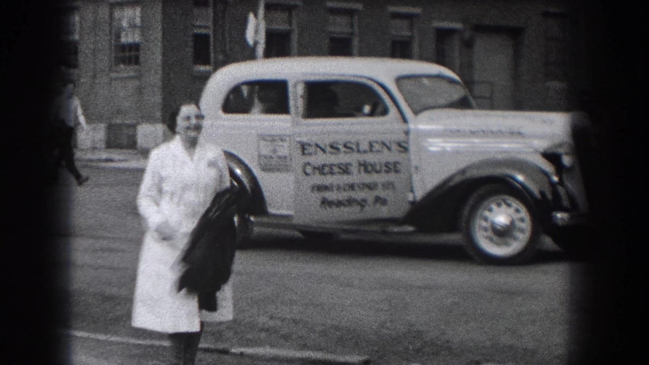 A woman in a light dress walks toward the camera while the Ensslen's Cheese House delivery car remains parked behind her.