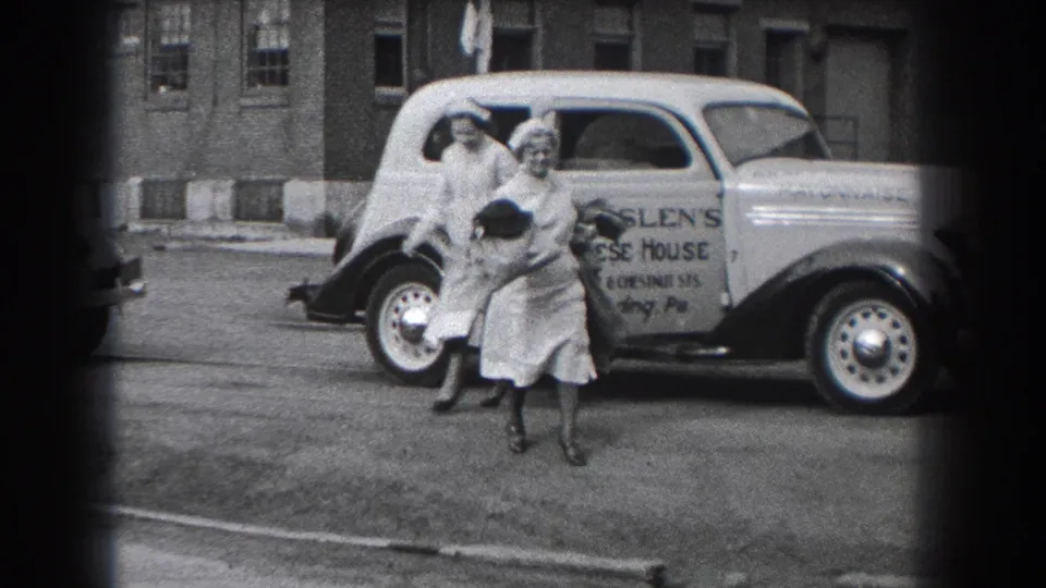 Two women are visible near the parked Ensslen's Cheese House delivery car, one facing the camera and another partly behind the vehicle area.