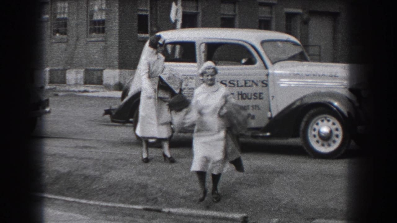 Two nurses in white uniforms and caps stand by a light-colored delivery car in Reading, Pennsylvania, in 1938.