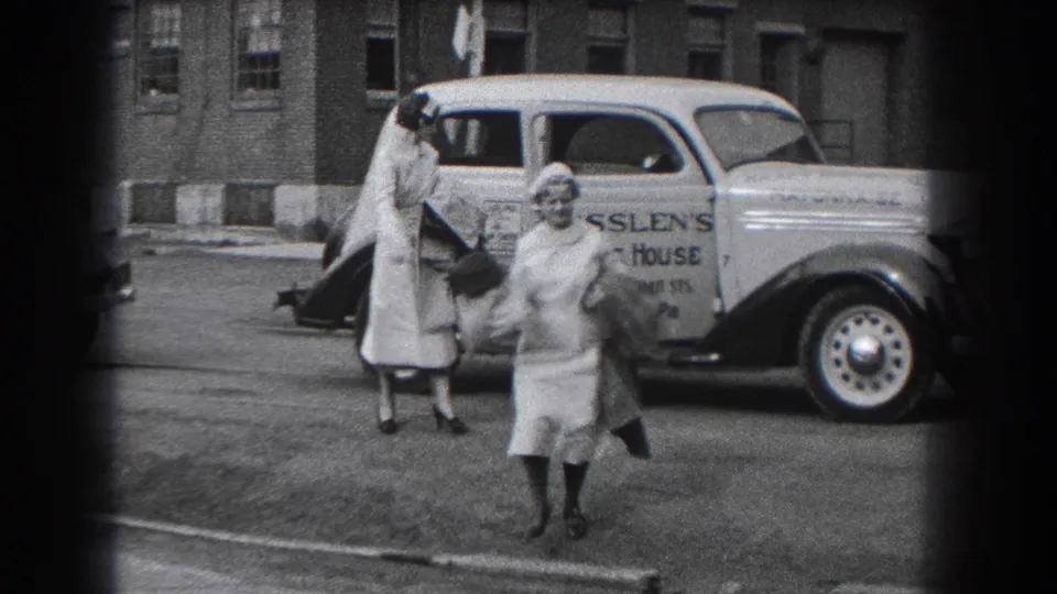 Two nurses in white uniforms and caps stand by a light-colored delivery car in Reading, Pennsylvania, in 1938.