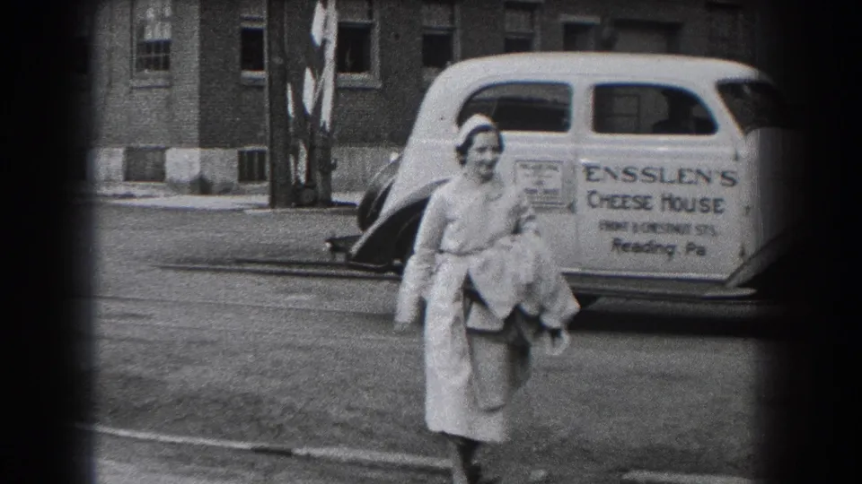 A nurse in a white uniform walks past an Enslen's Cheese House delivery car in Reading, Pennsylvania, in 1938.
