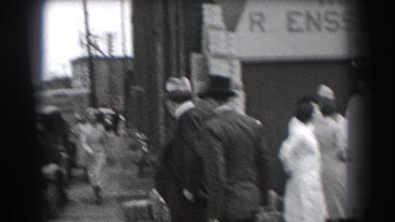 Adults stand on a sidewalk outside a brick storefront, with part of a business sign above them.