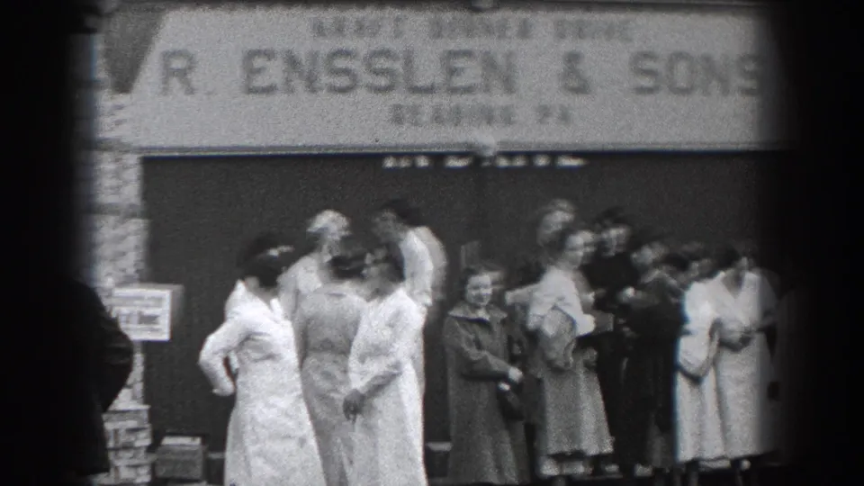 Adults in dresses, coats, and hats stand outside R. Ensslen & Sons in Reading, Pennsylvania, during a 1938 home-movie street scene.