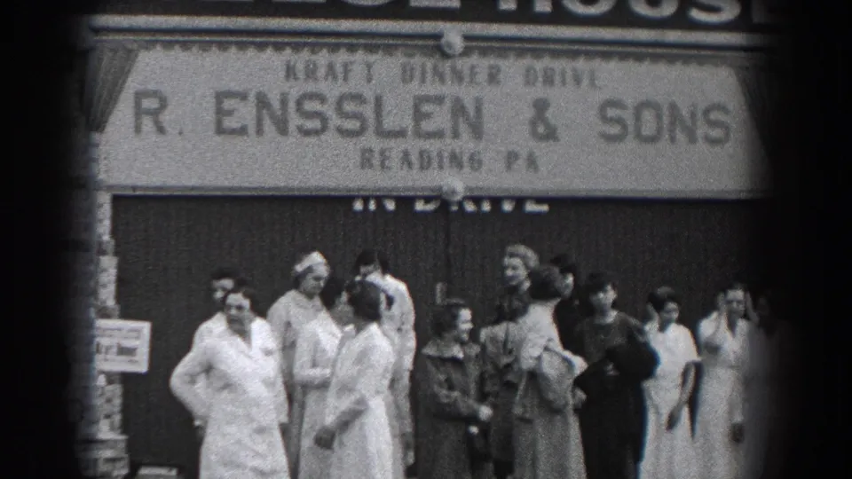 Adults stand and talk outside R. Ensslen & Sons in Reading, Pennsylvania, with the storefront sign and 1930s dress clearly visible.