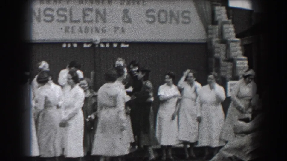 Black-and-white 8mm frame of people outside R. Ensslen & Sons in Reading, Pennsylvania, with the crowd spread across the sidewalk.