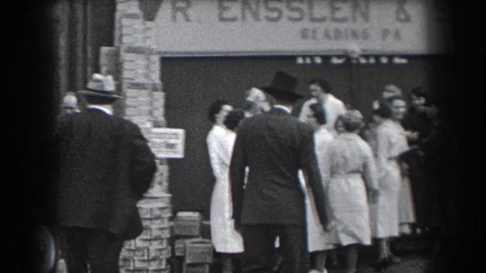 A suited man stands with his back to the camera as adults gather near the R. Ensslen & Sons storefront in 1938 Reading, Pennsylvania.