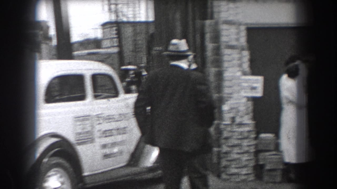 In Reading, Pennsylvania, a suited man in a fedora passes an Ensslen's Cheese House delivery car outside a commercial doorway.