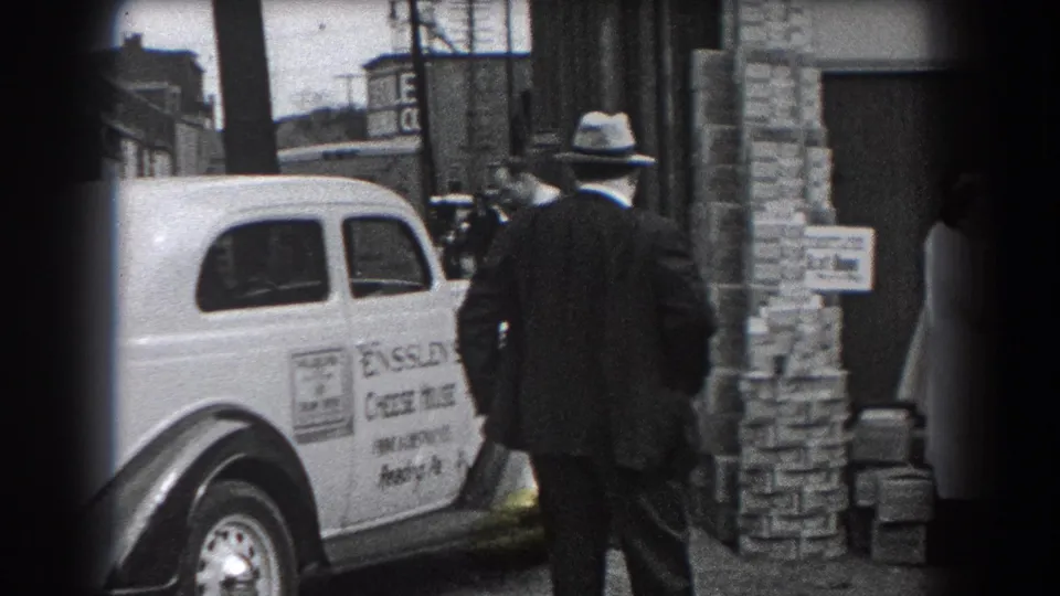 A Reading, Pennsylvania street view shows the Ensslen's Cheese House car beside a doorway, with a fedora-wearing man and bystanders nearby.