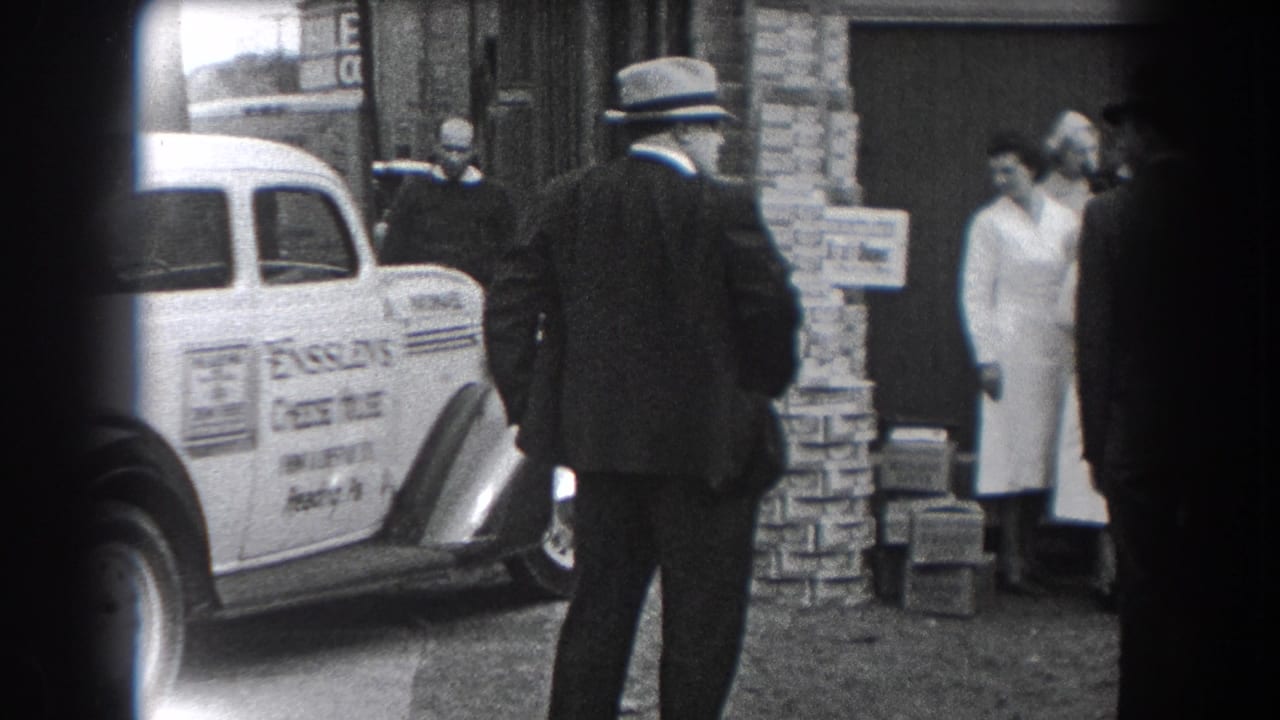 In 1938 Reading, Pennsylvania, a suited man faces a white Ensslen's Cheese House delivery car as people stand near a brick storefront.