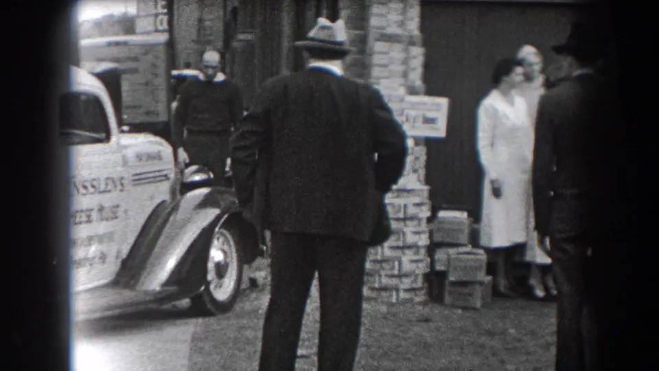 A man seen from behind watches people gathered by a brick building and a white cheese delivery car in Reading, Pennsylvania.