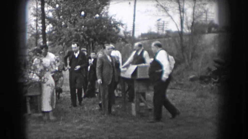 In Reading, Pennsylvania home-movie footage from 1938, adults in suits and dresses stand near an outdoor table on grass.