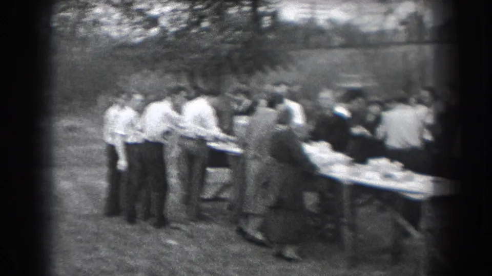 Adults gather around long outdoor tables with food or supplies in a soft-focus 1938 Reading, Pennsylvania home movie.