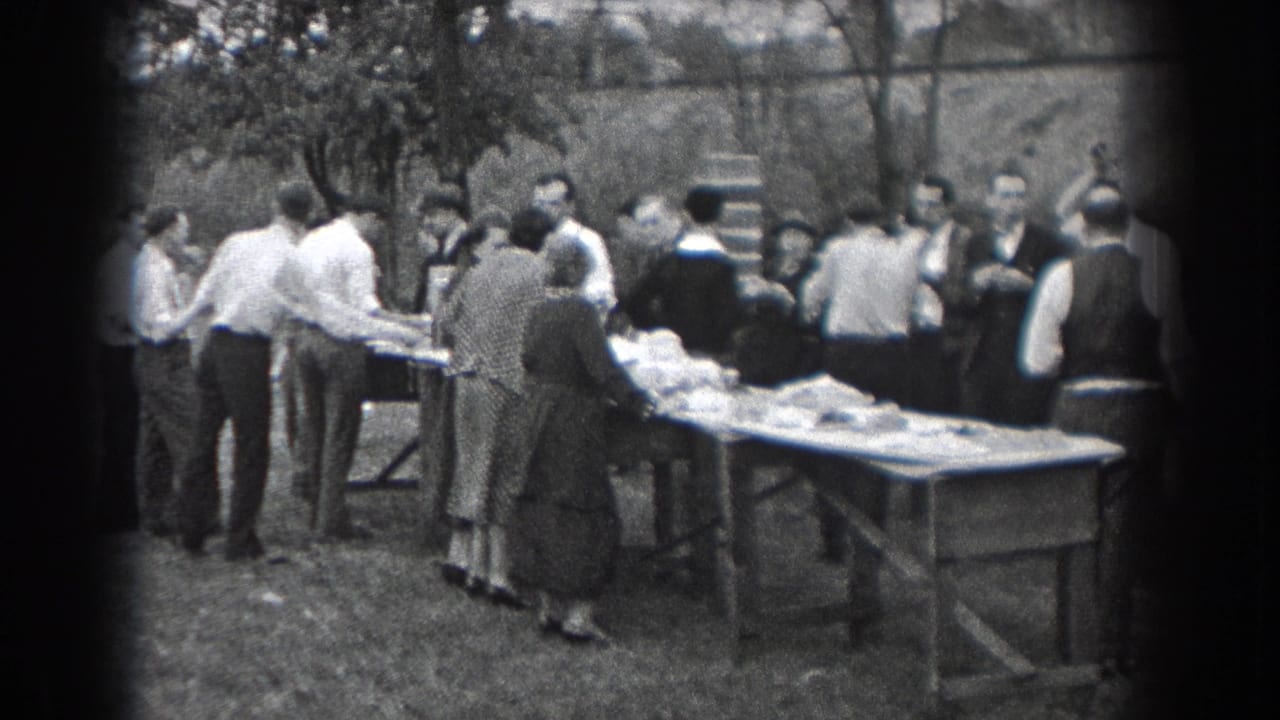 1938 Reading, Pennsylvania home-movie frame showing adults in period clothing gathered around food tables outdoors.