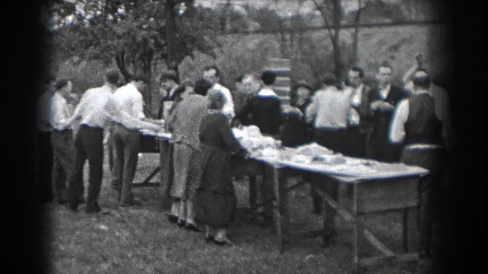 1938 Reading, Pennsylvania home-movie frame showing adults in period clothing gathered around food tables outdoors.