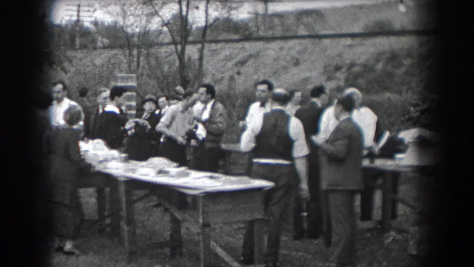 1938 home-movie still from Reading, Pennsylvania showing adults gathered tightly around a food table outdoors.