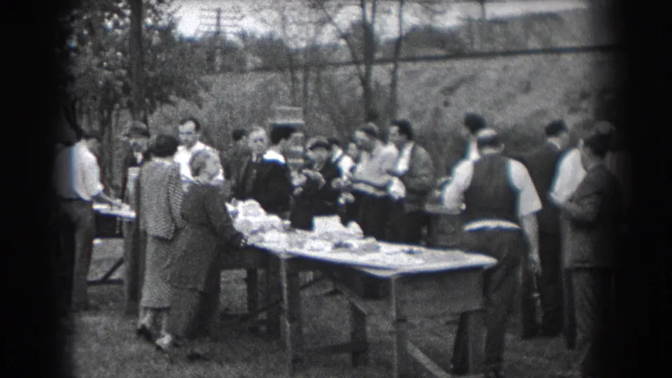 Reading, Pennsylvania 1938 home-movie frame with adults surrounding food tables in a grassy outdoor gathering.