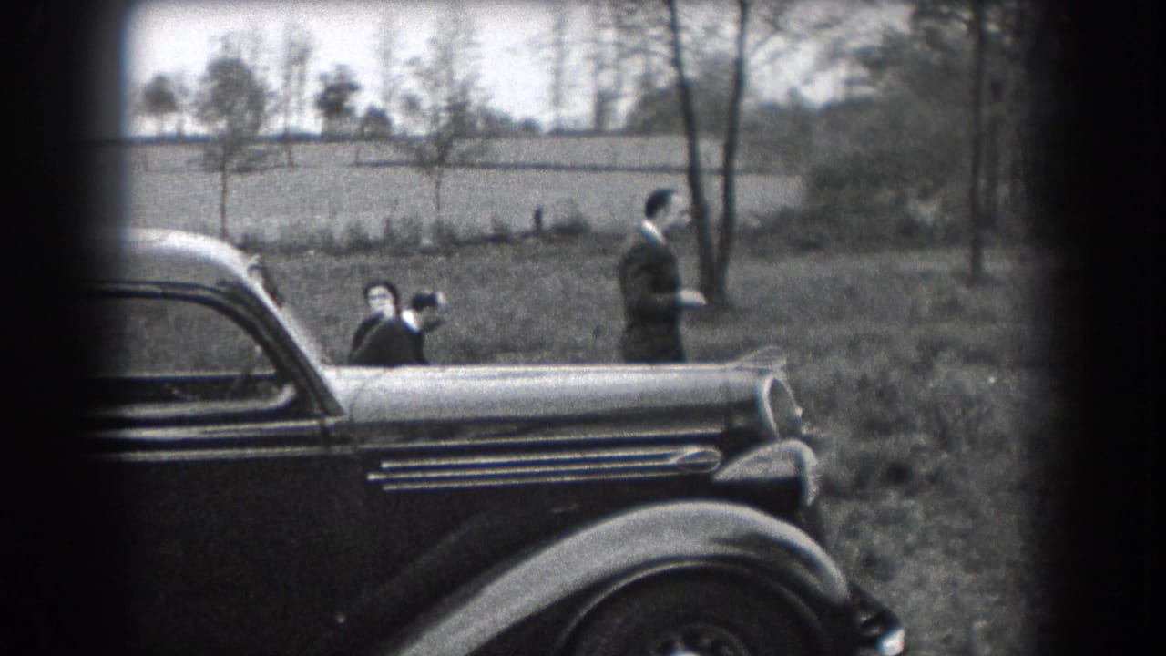 Adult men and a child stand near a dark vintage car in an open field.