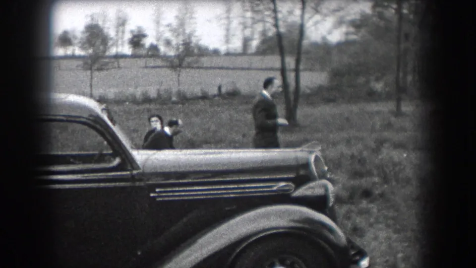 1938 Reading, Pennsylvania home-movie frame with two adult men and a child near a parked 1930s automobile in a grassy outdoor area.