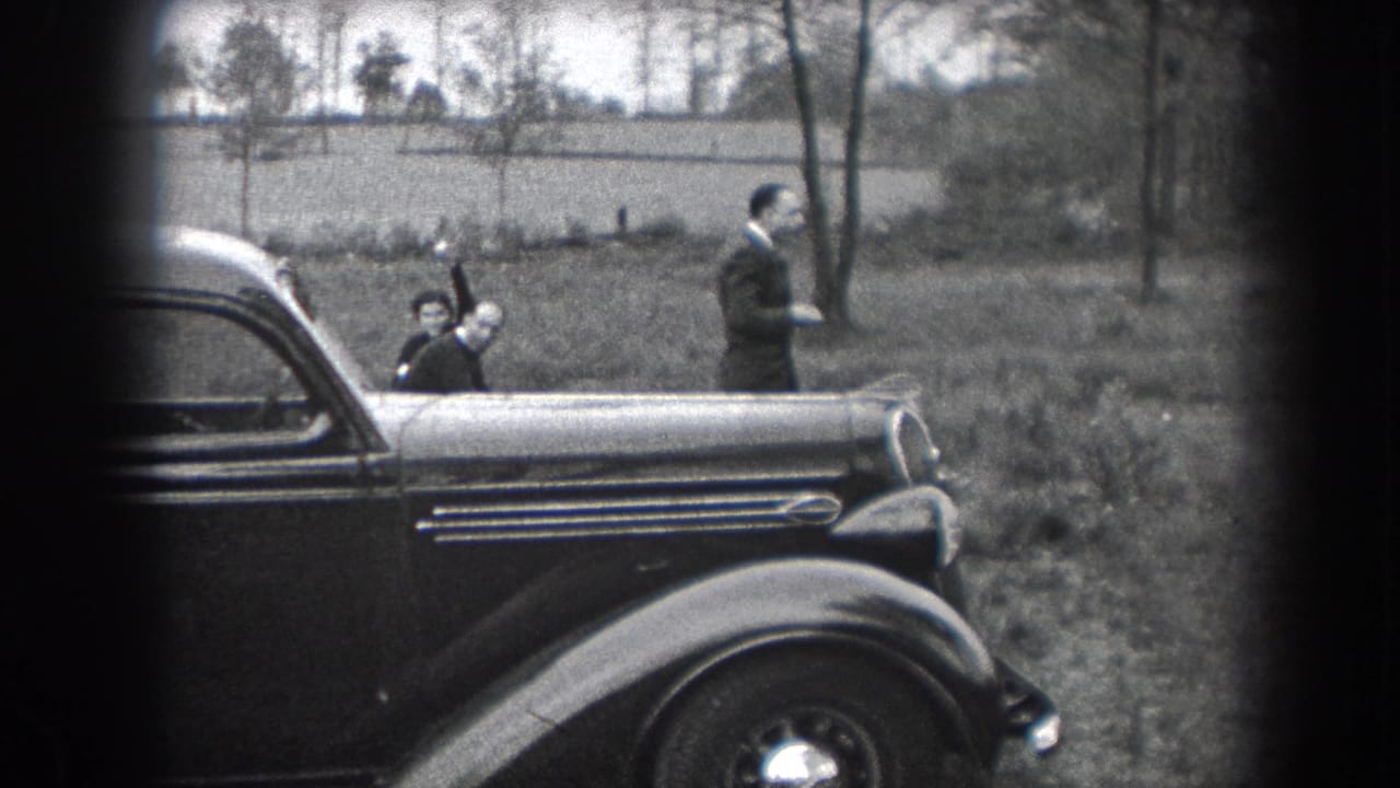 A child waves beside a parked vintage car while an adult man stands nearby.