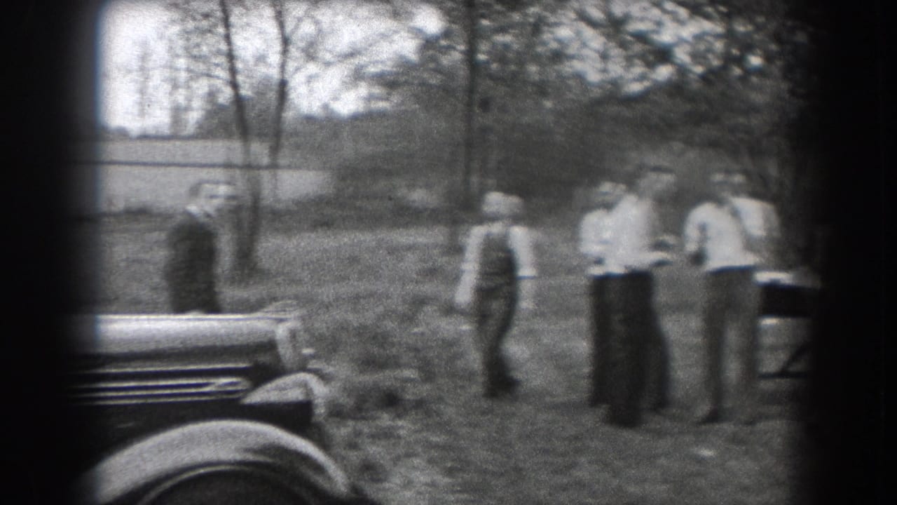 In 1938 Reading, Pennsylvania, adults in period clothing gather on a lawn near parked cars and trees.