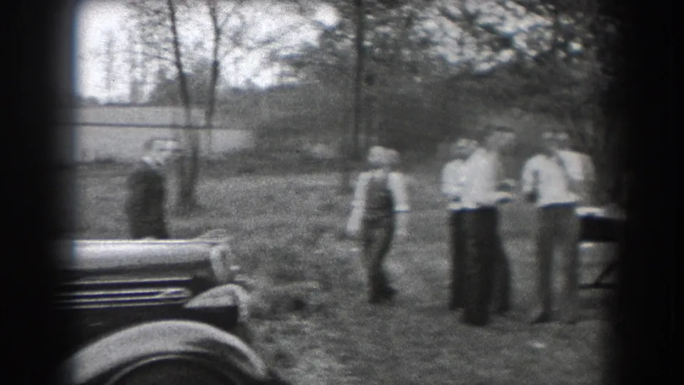In 1938 Reading, Pennsylvania, adults in period clothing gather on a lawn near parked cars and trees.