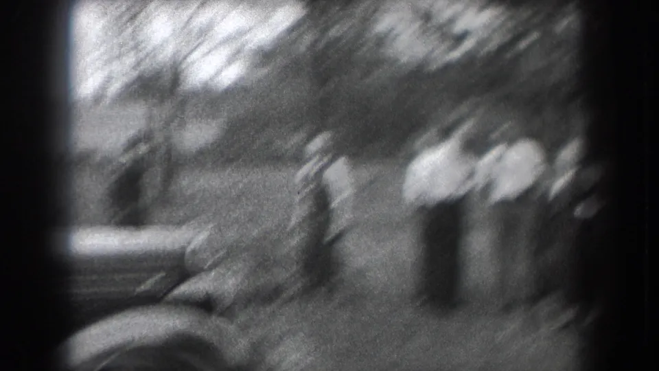 Soft 8mm frame from Reading, Pennsylvania, showing adults grouped near a parked car in an outdoor setting.