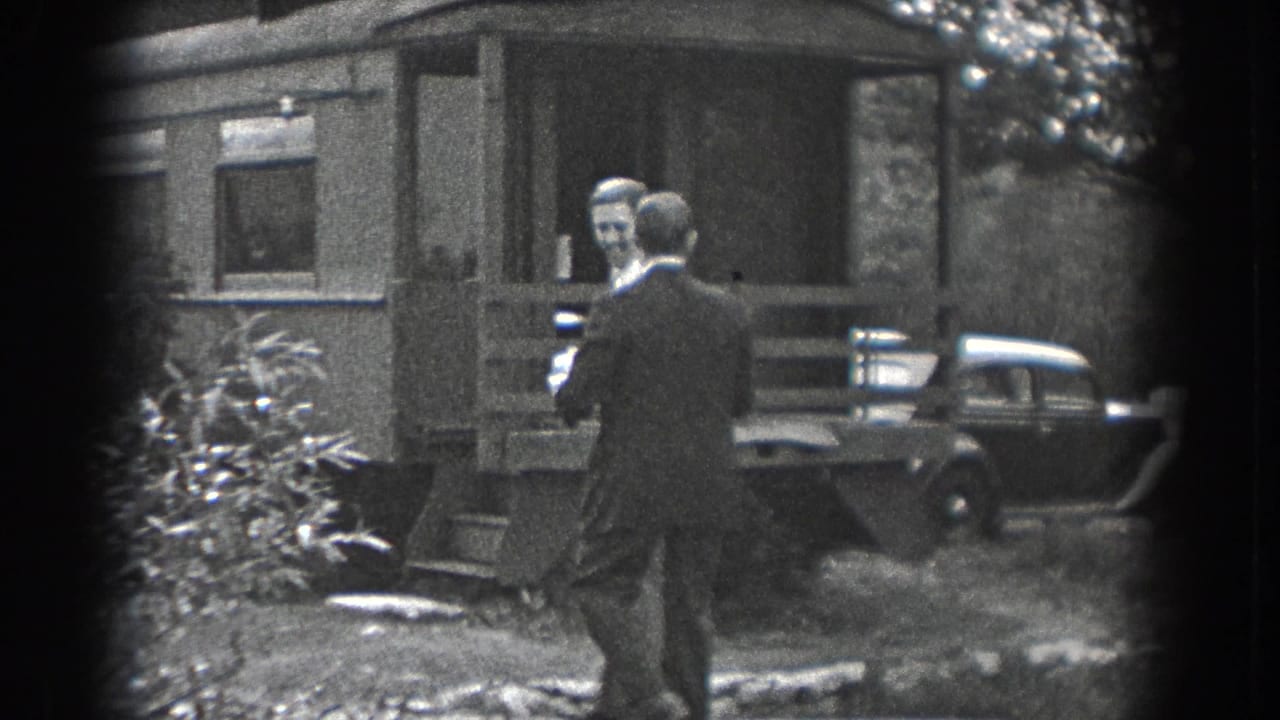 In 1938 Reading, Pennsylvania, two adult men approach a modest house near shrubs and a parked period automobile.