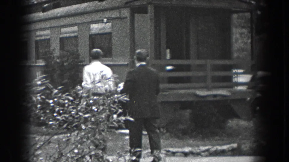Two adult men in 1938 Reading, Pennsylvania walk toward a modest porch, with shrubs and a parked car in the yard view.