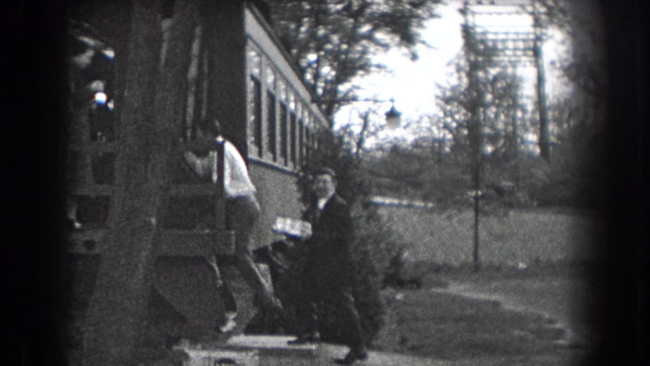 Two men near a house exterior, one stepping down while another holds a cake or tray.